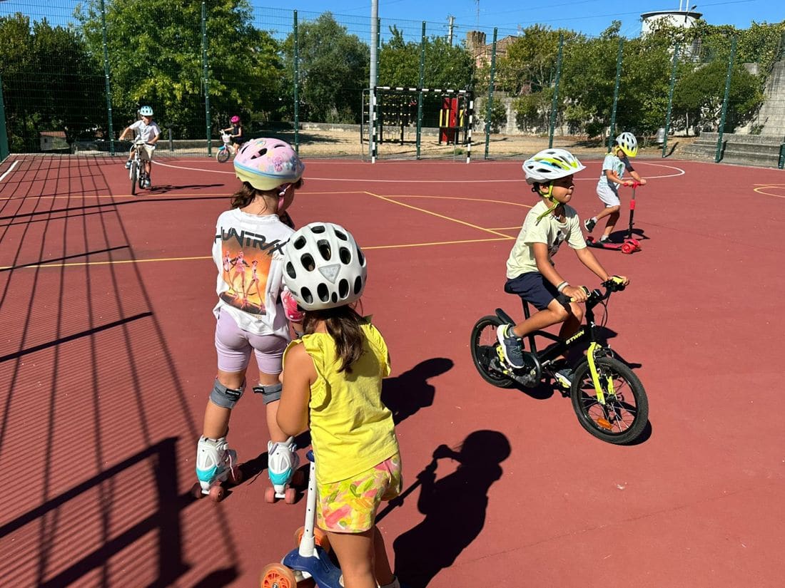 Crianças de capacete a andar de bicicleta e patins no recreio
