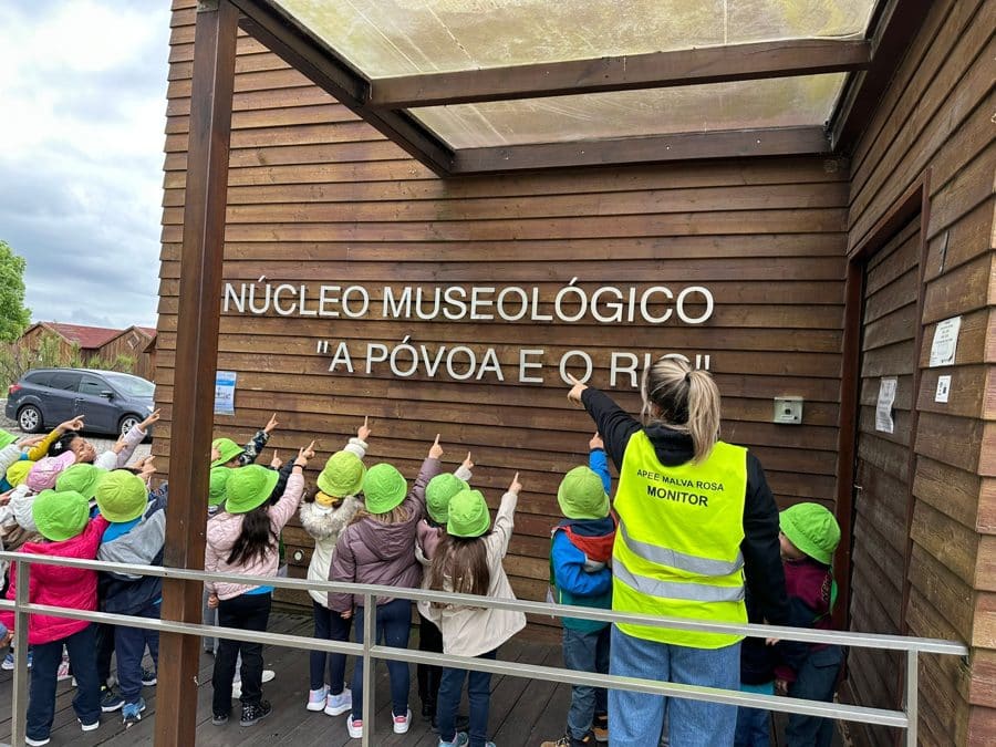 Grupo de crianças de chapéu verde, de costas, à entrada de um museu